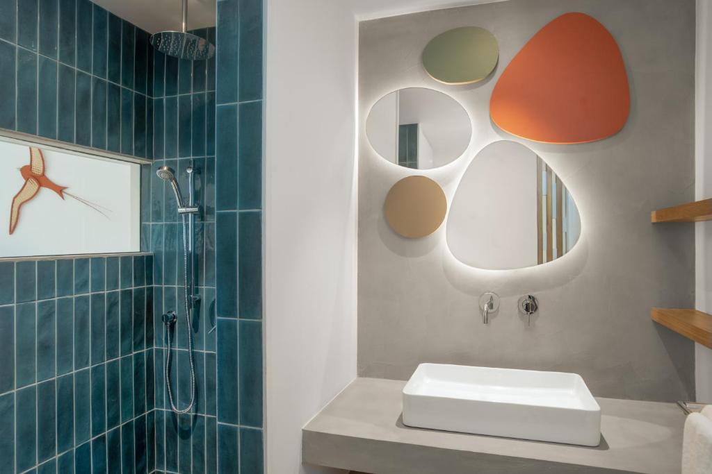 Mūsdienīga vannas istaba ar zaļiem flīzēm, dušu un dekoratīvām spoguļu formām. Interjeru papildina minimālistiska izlietne un dabīgas krāsas akcenti.