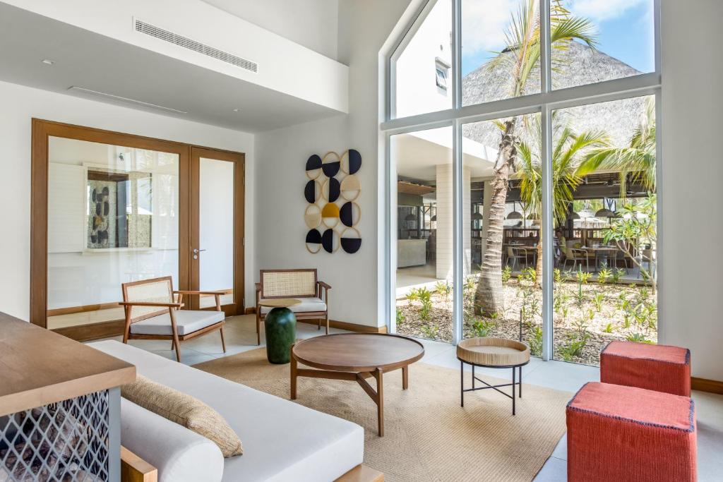 Mūsdienīgs viesistabas interjers ar lieliem logiem, kas ved uz dārzu, un stilīgām mēbelēm, piemēram, koka krēsliem un galdiem. Daba un gaisma rada patīkamu atpūtas atmosfēru.