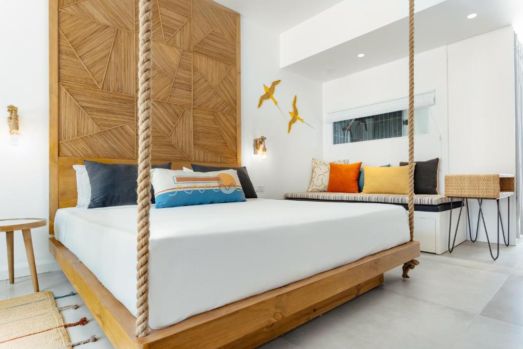 Mūsdienīgs guļamistabas interjers ar piekārto gultu no koka, rotātu ar ģeometrisku koka paneļa sienu un spilveniem dažādās krāsās. Telpā ir arī gaismas elementu un dekoratīvu putnu akcenti.