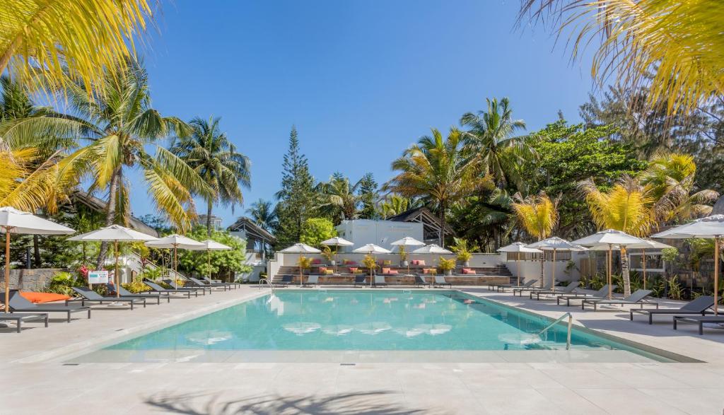 Lieliska atpūtas zona ar baseinu, apjoztu ar palmām un sauļošanās krēsliem, ideāla relaksācijai saulainā dienā. Šī ainava rada mierīgu atmosfēru un viesmīlību.