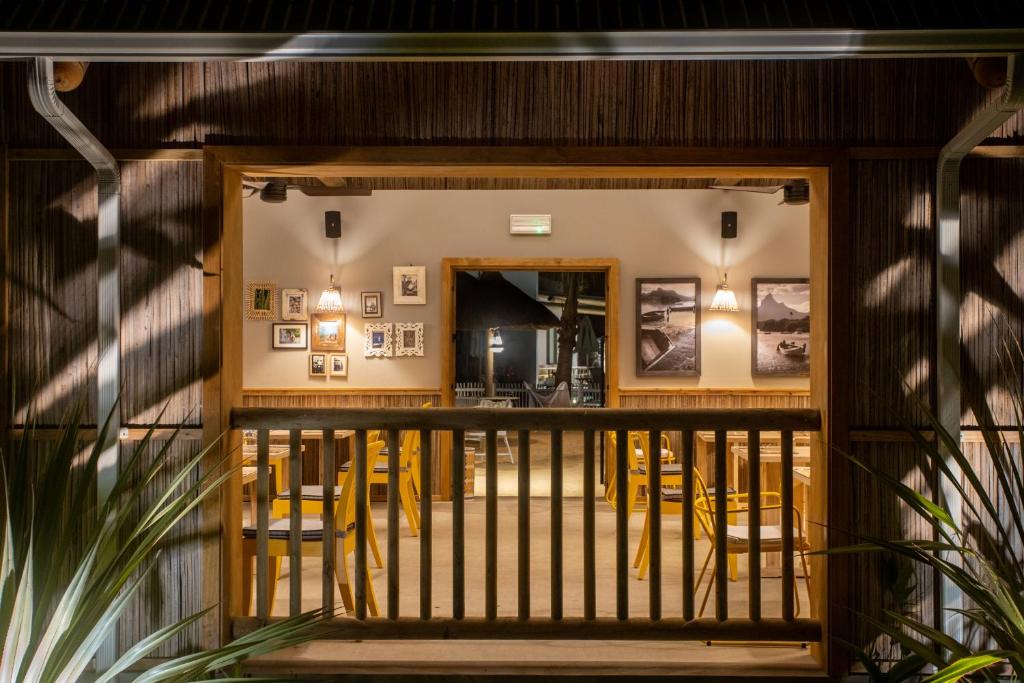 Restorāna interjers ar siltu apgaismojumu un dekoratīvām fotogrāfijām uz sienām, redzams caur koka terases balkonu. Sēdvietas ir ar dzeltenām krēsliem, radot viesmīlīgu atmosfēru.