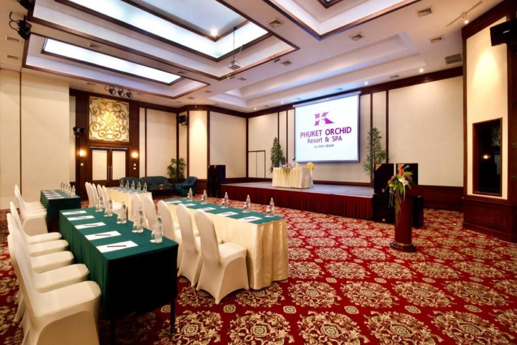 Konferences zāle Phuket Orchid kūrortā un SPA, ar zaļiem galdiem un baltām krēslām, piedāvā modernu vidi sanāksmēm un pasākumiem. Uz ekrāna redzams kūrorta nosaukums.