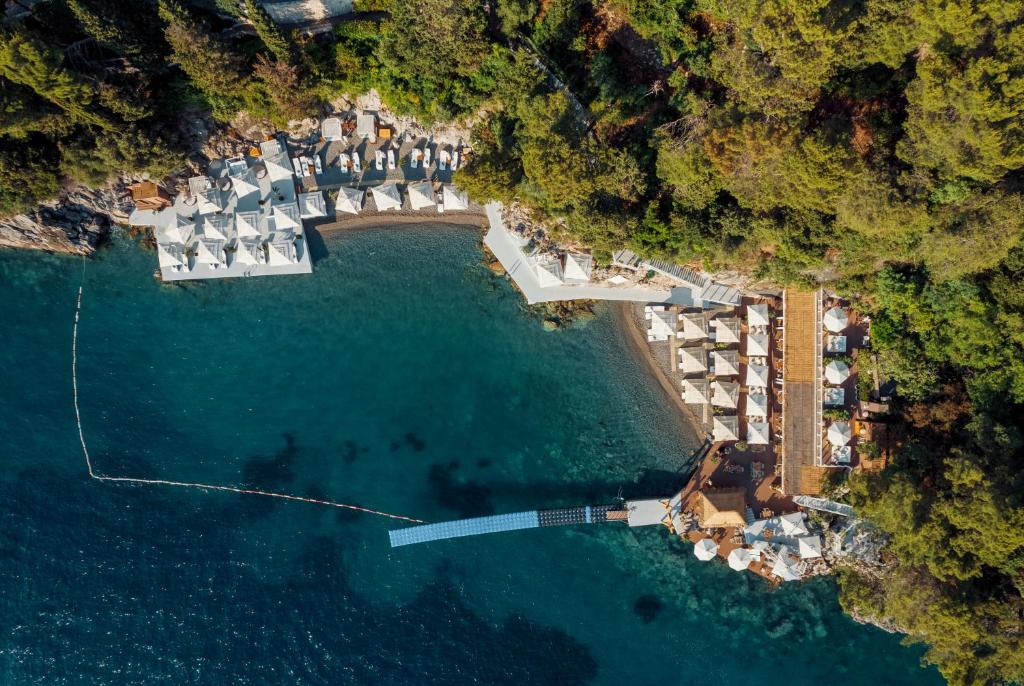 Pārskats uz piekrastes kūrortu ar baltiem teltīm un zilu ūdeni, ko ieskauj zaļi koki. Ideāla vieta atpūtai un relaksācijai.