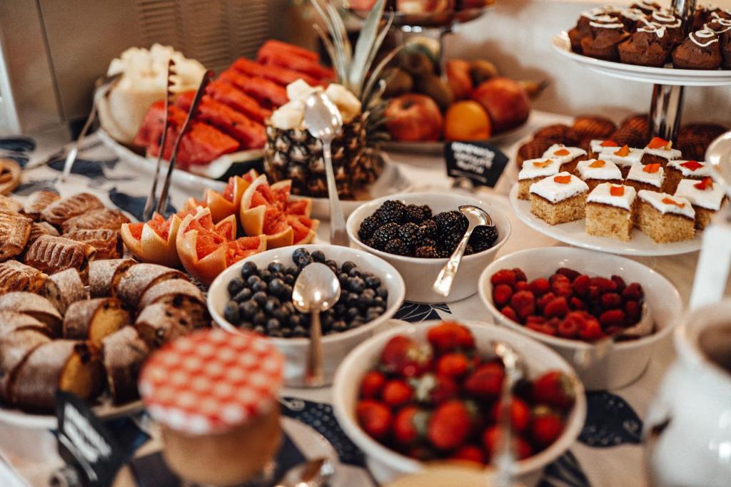 Bagātīgs augļu un desertu bufete ar dažādām delikatesēm, tostarp zemenēm, mellenēm, avenes un kūkām. Ideāli piemērota svinībām vai brokastīm.