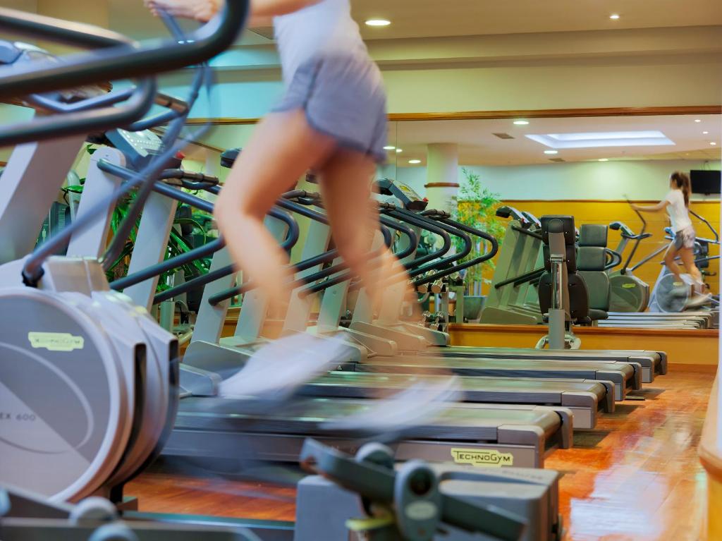 Sporta zāles apmācība ar eliptiskajiem trenažieriem, kur cilvēki aktīvi vingro. Spogulī redzams otrais vingrotājs.