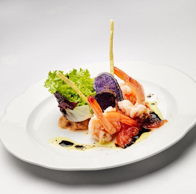 Gatavu garneles ēdienu ar krāsainiem dārzeņiem un dekoratīvām piedevām uz baltā šķīvja.