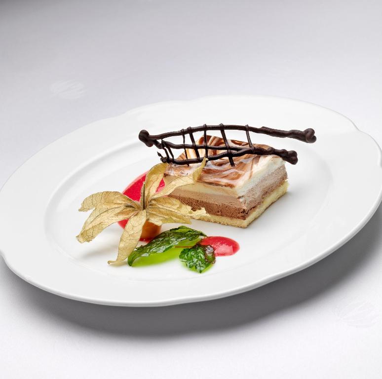 Saldais deserts ar trīs kārtām, dekorēts ar šokolādes režģi un zeltainu lapu, pasniegts ar augļu mērci.