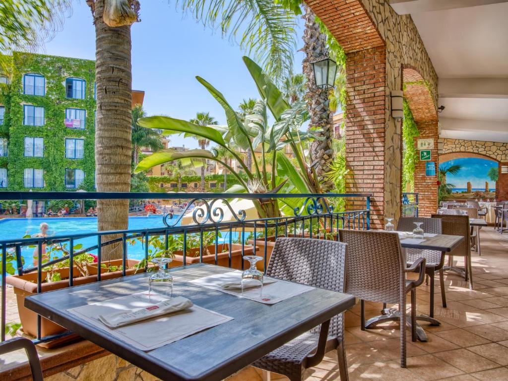 Terases restorāns ar skatu uz peldbaseinu, kurā ir zaļumi un palmām, radot relaksējošu atmosfēru. Interjers ir elegants ar galdiem un krēsliem, gataviem viesiem.