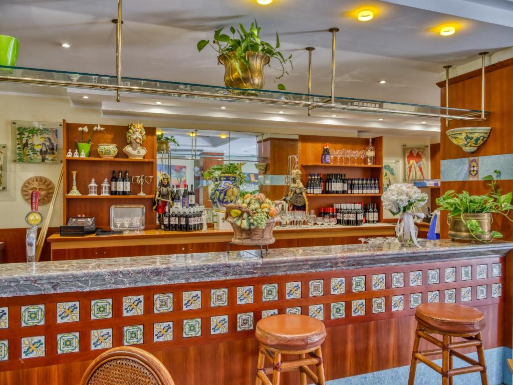 Mūsdienīgs bārs ar elegantu interjeru, dekorēts ar krāsainām flīzēm un dažādiem mākslas elementiem. Skats uz bāra letes daļu ar dzērieniem un augļiem, radot viesmīlīgu atmosfēru.