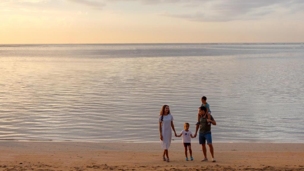 Ģimene pastaigā pa pludmali saulrietā, baudot mierīgu jūras ainavu. Attēls atspoguļo laimīgas brīvdienas un kopā būšanu.