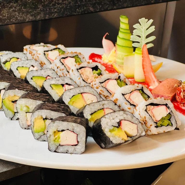 Svaigu suši šķēles ar avokado, nori un krabju gaļu, dekorētas ar dārzeņu rotājumiem.