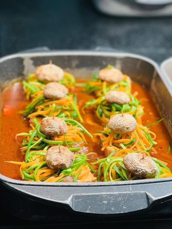 Svaigu dārzeņu un sēņu ēdiens, kas gatavots ar aromātisku mērci, pasniegts cepšanas traukā.