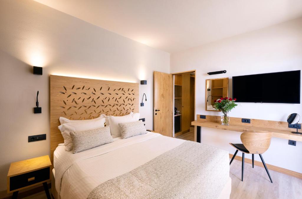 Mūsdienīga guļamistaba ar koka akcentiem, ērtu gultu un televizoru. Telpā ir arī rakstāmgalds ar ziedu kompozīciju un elegantu krēslu.