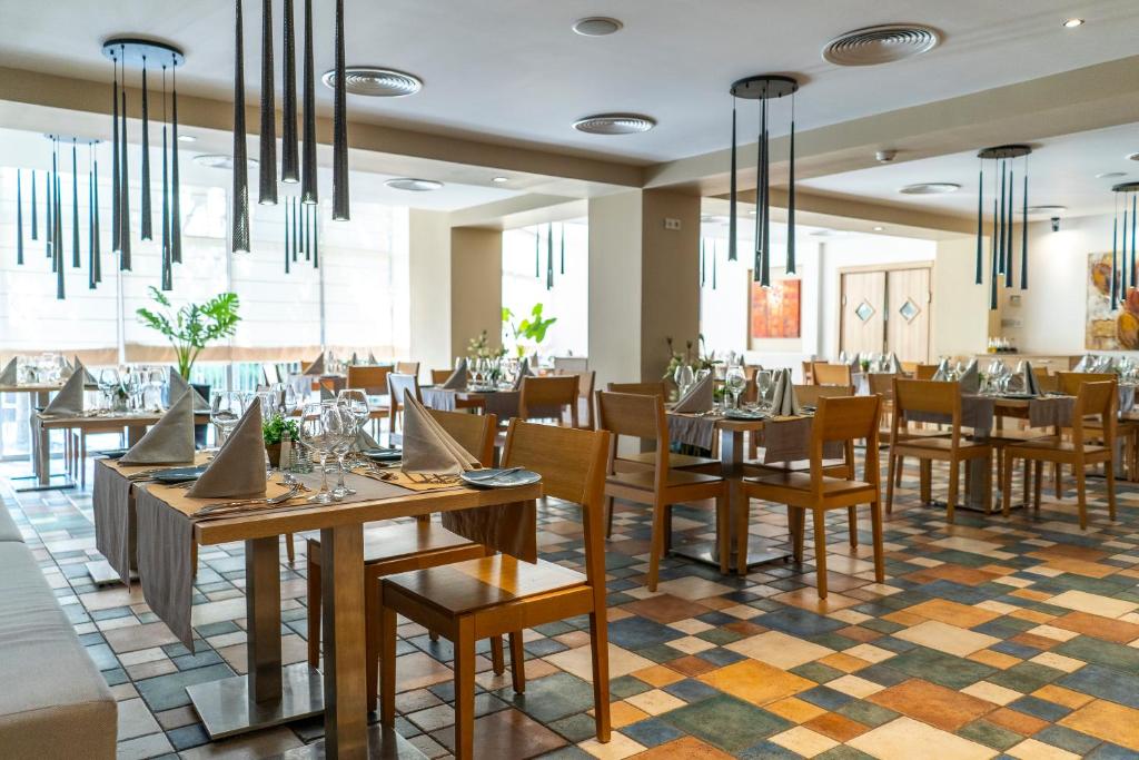 Mūsdienīga restorāna interjers ar koka galdiem un krēsliem, eleganti galdauti un stikla trauki. Telpā ir daudz gaismas un dekoratīvi elementi.