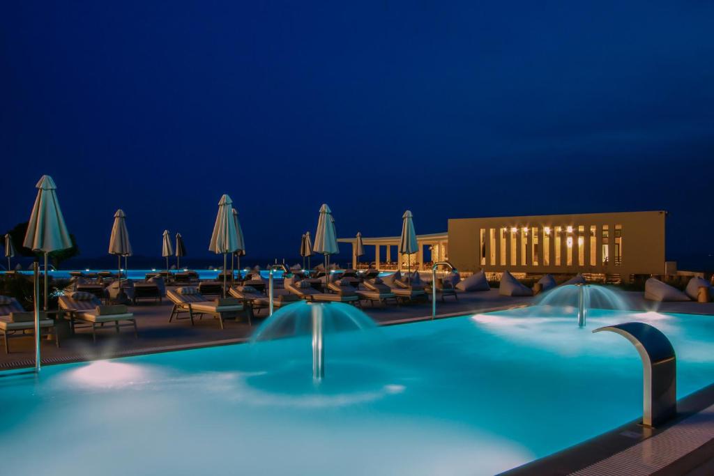 Elegants baseins ar strūklakām un sauļošanās krēsliem, apgaismots naktī, radot relaksējošu atmosfēru. Paviljons fona piebilst modernu šarmu.