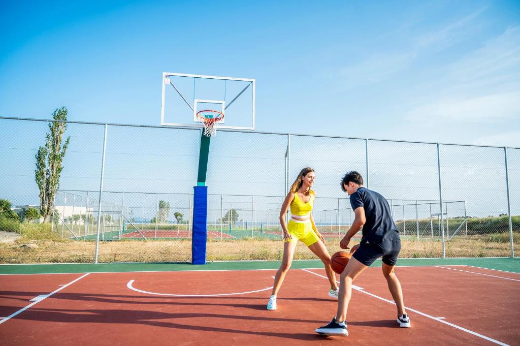 Divi cilvēki spēlē basketbolu uz sporta laukuma, viens no viņiem ir tērpies dzeltenā sporta apģērbā, bet otrs - tumšā. Fons parāda tīklu un basketbola grozu zem saulainas debess.