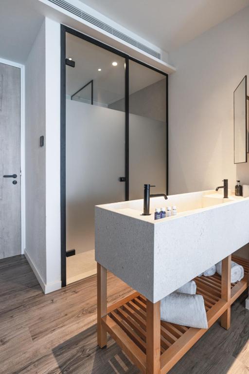 Mūsdienīgs vannas istabas dizains ar akmens izskata izlietni uz koka statīva un stikla dušas kabīni. Eleganta un minimālistiska atmosfēra.