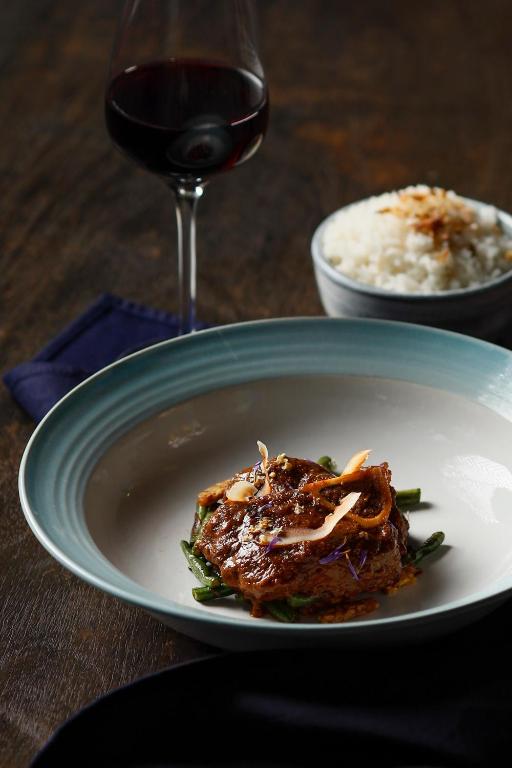 Gurķu salāti ar marinētu gaļu, rīsiem un sarkanvīna glāzi, uz tumša galda.
