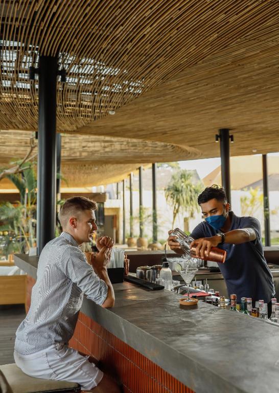 Bāra apkalpošana, kur bārmenis sajauc kokteili, kamēr klients ar interesi raugās. Moderns un stilīgs bārs ar koka elementiem un zaļumiem apkārt.