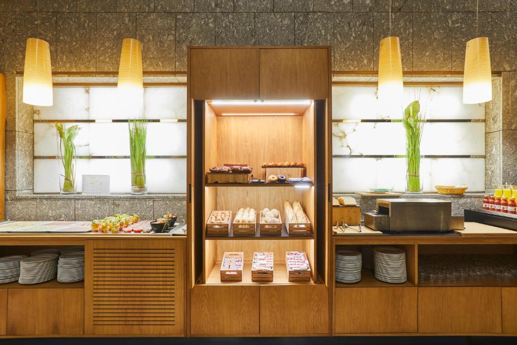 Kafijas bārs ar modernu interjeru, kurā redzami dažādi konditorejas izstrādājumi, augļu šķīvji un dekoratīvi elementi. Apgaismojums rada patīkamu atmosfēru, padarot to par ideālu vietu brokastīm vai uzkodām.