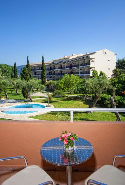 Skats uz viesnīcu ar dārzu un baseinu no balkona, uz galdiņa ziedu pušķis.