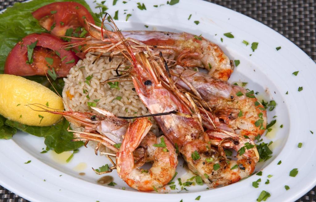 Garšīgas garneles, pasniegtas uz rīsu gultas ar citronu, tomātu un salātu lapām, dekorētas ar svaigiem pētersīļiem.