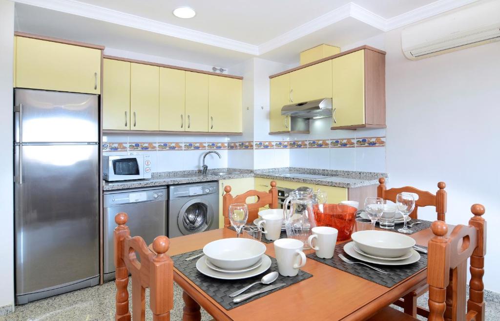 Mūsdienīga virtuve ar dzeltenām mēbelēm un galdu, kas klāts ar galda piederumiem. Virtuvē ir moderni iekārtas, tostarp ledusskapis, mikroviļņu krāsns un veļas mašīna.