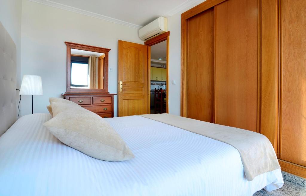 Mūsdienīgs guļamistabas interjers ar gultu, spilvenu un koka mēbelēm. Telpā ir gaismas spuldze un spogulis, kas piešķir siltu atmosfēru.