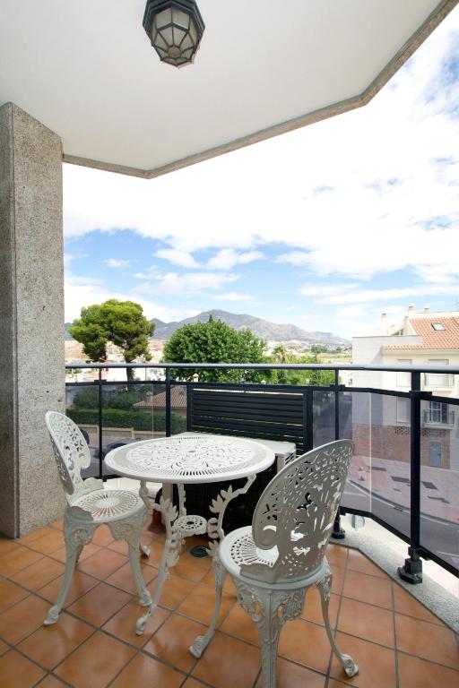 Balkons ar metāla galdu un krēsliem, no kura paveras skats uz kalniem un apkārtējo ainavu. Gaisma ieplūst caur logiem, radot patīkamu atmosfēru.