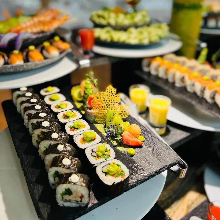 Svaigu sushi un siera šķīvji, kas sakārtoti uz melnas akmens plāksnes, dekorēti ar dārzeņiem un augļiem. Šī elegantā prezentācija nodrošina pievilcīgu ēdienu pasniegšanas veidu.