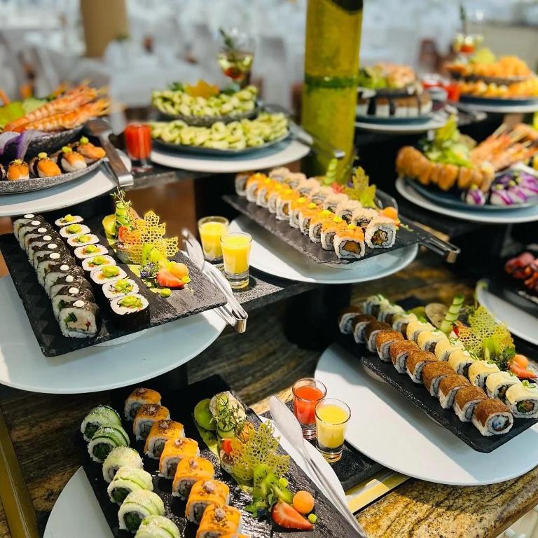 Svaigu sushi dažādība uz eleganta galda, ietverot krāsainus rullīšus, garneles un augļu dzērienus. Ideāla izvēle sushi mīļotājiem.