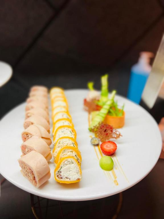 Skaisti pasniegti sushi un rullīši uz balta šķīvja, dekorēti ar dārzeņiem un augļiem. Rūpīgi sakārtoti, radot krāsainu un pievilcīgu ēdiena kompozīciju.