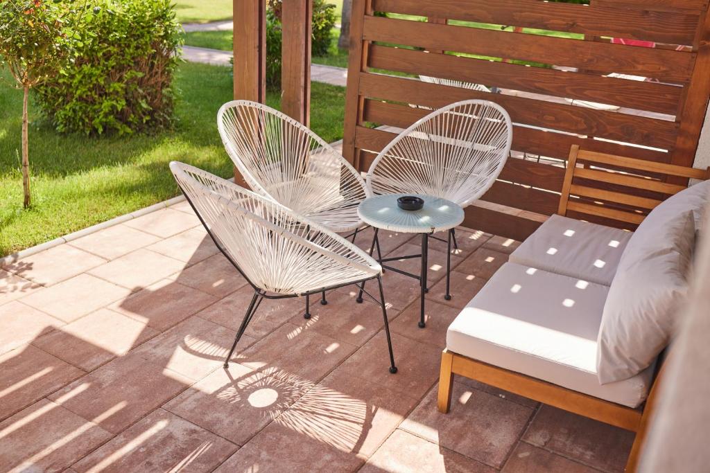 Mūsdienīga terases zona ar baltiem sēdekļiem un kafijas galdiņu, kurā ir pievilcīga atpūtas atmosfēra. Daba apkārt papildina relaksējošo vidi.