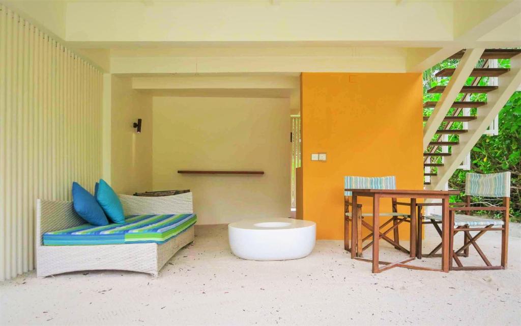 Mūsdienīgs atpūtas stūris ar krāsainu dīvānu, baltu kafijas galdiņu un koka galdu ar krēsliem, kas atrodas gaišā telpā ar dabiskiem elementiem.