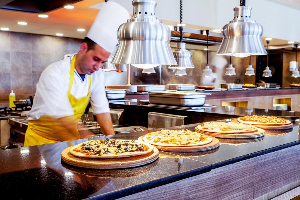 Picas šefpavārs gatavo ēdienus modernā restorānā, ar vairākām pīrāgu plāksnēm uz letes. Gaisma un interjers rada viesmīlīgu atmosfēru.