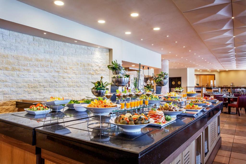 Bagātīgs bufetes galds ar dažādiem ēdieniem, ieskaitot salātus, uzkodas un dzērienus, modernā restorāna interjerā. Ideāli piemērots svinībām un īpašiem pasākumiem.