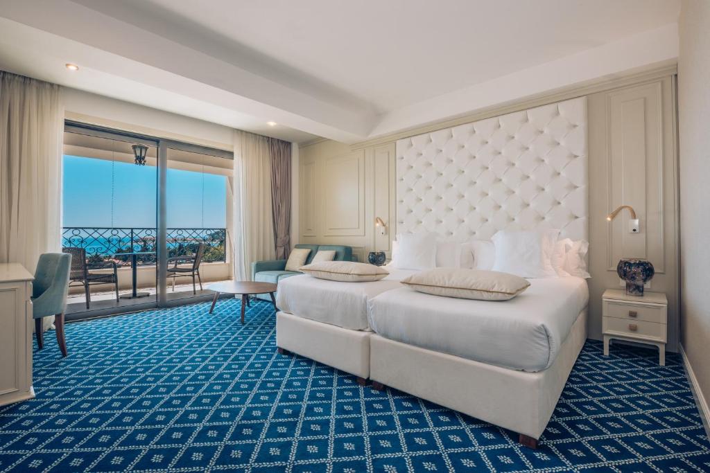 Luksusa viesnīcas numurs ar divām gultām, modernu interjeru un balkonu, kas paver skatu uz jūru. Eleganti izstrādāta telpa ar zilu paklāju un dabiskiem gaismas avotiem.