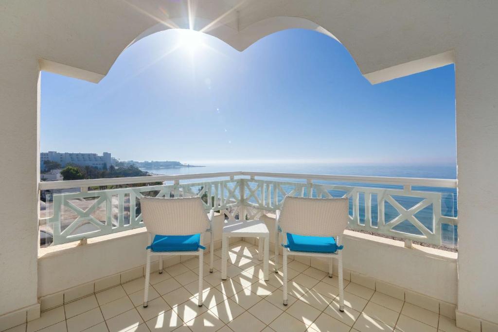 Saulaina terase ar divām baltām krēslu sēdvietām un skatu uz jūru, radot mierīgu un relaksējošu atmosfēru. Ideāls brīvdienu galamērķis.