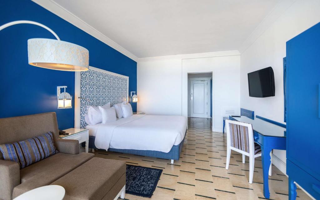 Mūsdienīgs viesnīcas numurs ar zilu sienu, divām gultām, dīvānu un darba galdu. Interjerā ir eleganti apgaismojuma elementi un koka grīda.