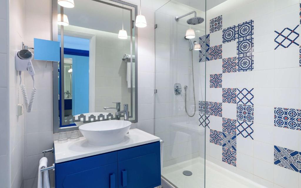 Mūsdienīga vannas istaba ar stikla dušu, balto izlietni un zilo skapīti, rotāta ar krāsainiem flīzēm. Svaiga un stilīga vide, ideāla relaksācijai.