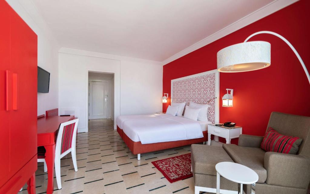 Mūsdienīgs viesnīcas numurs ar sarkanu sienu, baltu gultu un modernu mēbeļu dizainu. Telpā ir rakstāmgalds, televizors un ērta atpūtas zona.