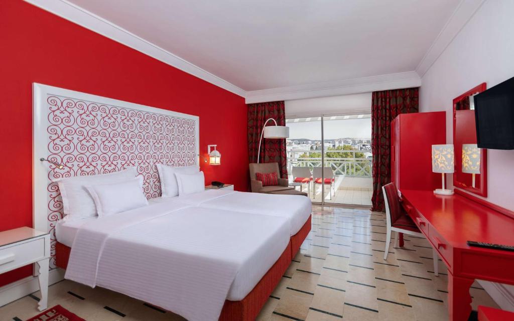 Mūsdienīgā viesnīcas numurā ar sarkaniem akcentiem ir divas gultas, rakstāmgalds un balkons ar skatu. Telpā ir arī televizors un komfortabla atpūtas zona.