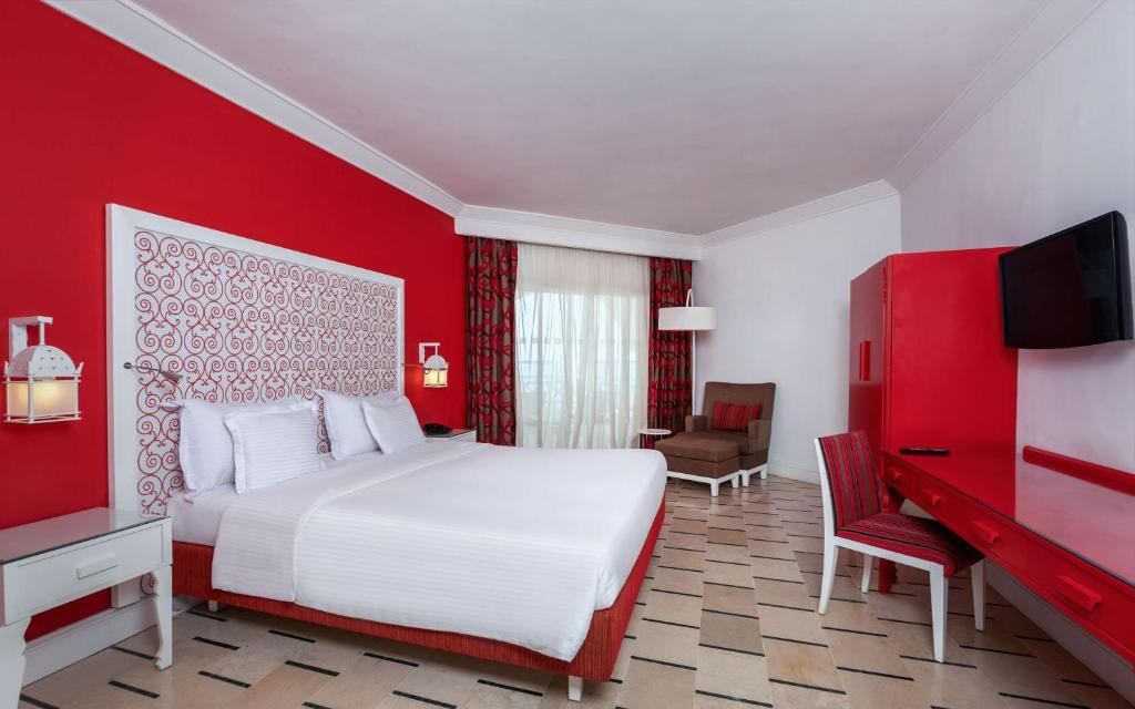 Mūsdienīga viesnīcas numura iekārtojums ar sarkaniem akcentiem, plaša gulta un ērta atpūtas zona. Numurā ir lieli logi, kas nodrošina dabisko apgaismojumu.