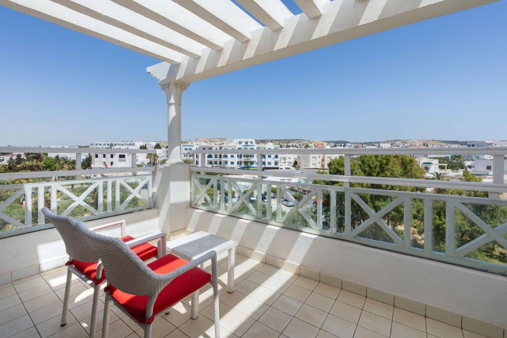 Patiņš ar divām sarkanu krēslu komplektu un galdu, kas atrodas uz balkona ar skatu uz apkārtni un skaidru debesi.