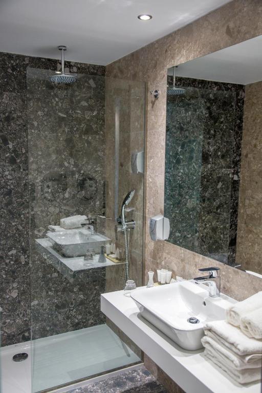 Mūsdienīgs vannas istabas interjers ar stikla dušu, elegantu izlietni un kvalitatīvu apgaismojumu, radot elegantu un relaksējošu atmosfēru.