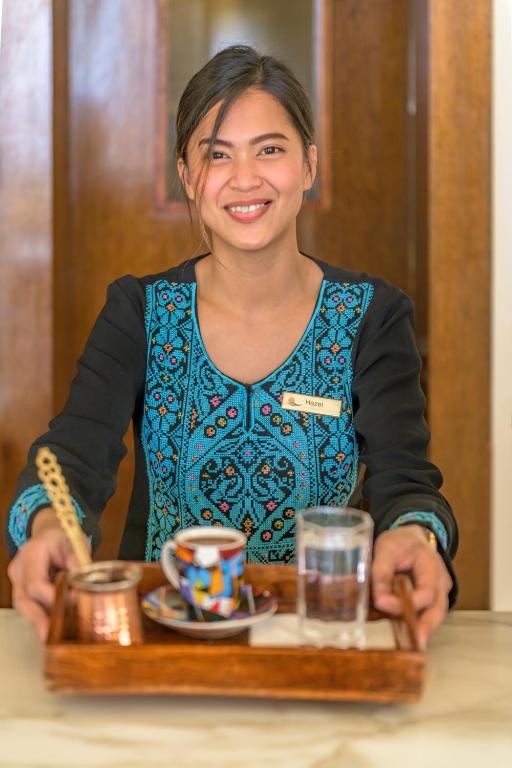 Smaids viesmīlis pasniedz kafijas un ūdens pasniegšanas tray, tērpies tradicionālā apģērbā ar krāsainu izšuvumu.
