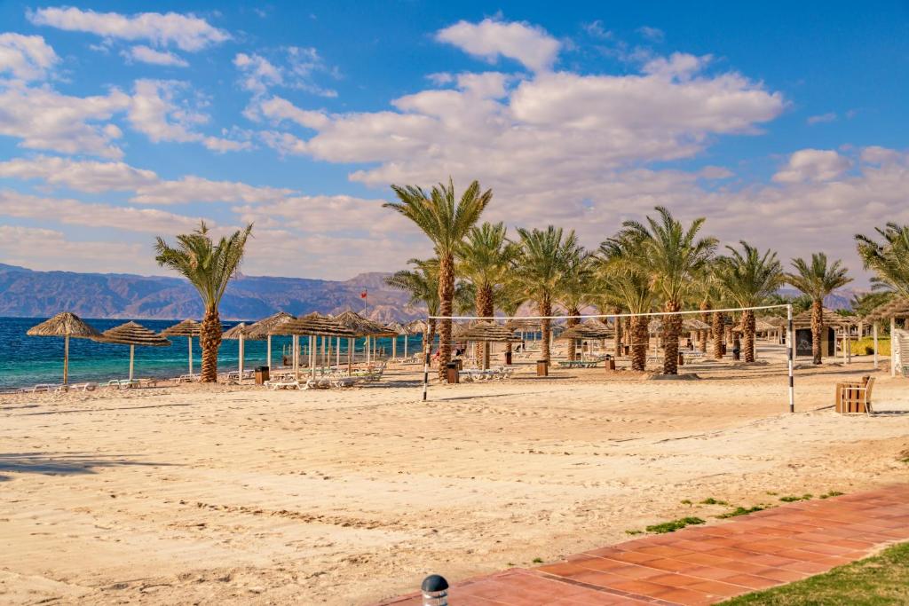 Pludmale ar palmām un volejbola tīklu, mierīgs skats uz jūru ar kalniem fona. Ideāla vieta atpūtai un sportiskām aktivitātēm.