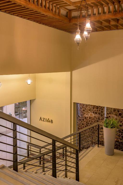 Mūsdienīga kāpņu telpa ar gaismas ķermeņiem un koka griestiem, kurā redzama nosaukuma zīme "AZIAB" un zaļa auga pods.