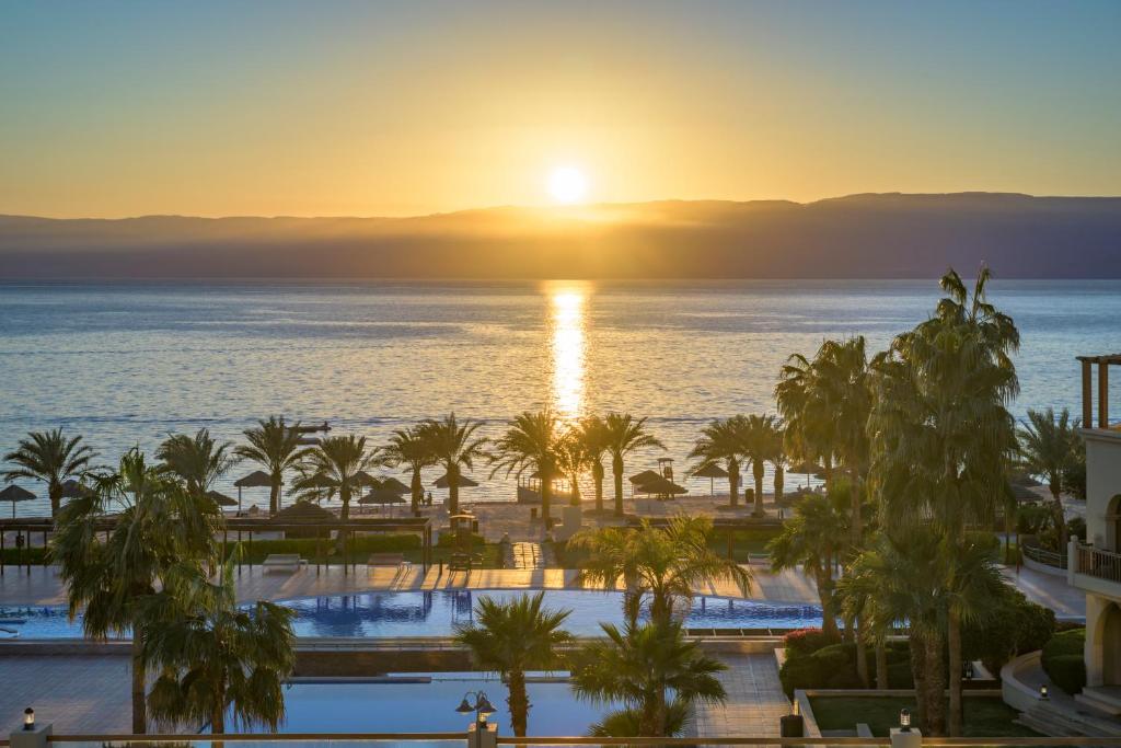 Saulriets virs ūdens, ar palmu rindām un baseinu priekšplānā, radot mierīgu un relaksējošu atmosfēru.