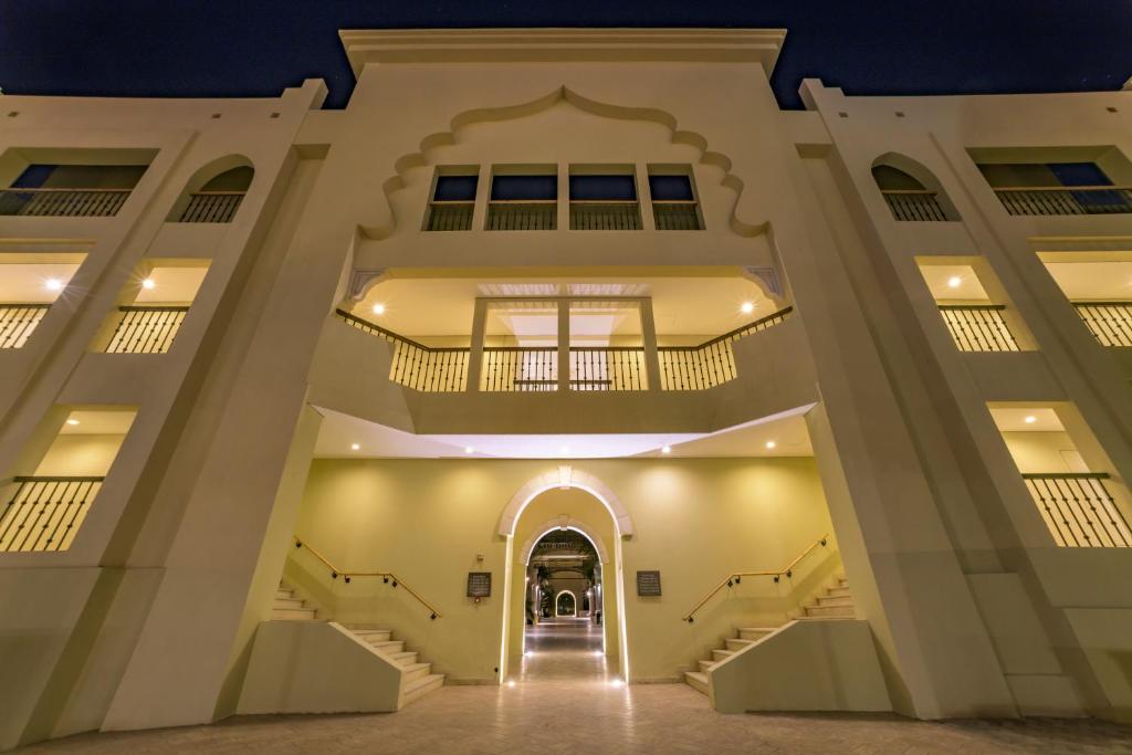 Eleganta arhitektūra ar izgaismotiem stāviem un plašu ieeju, kas rada viesmīlīgu atmosfēru. Vakarā redzamā gaisma uzsver ēkas detaļas.